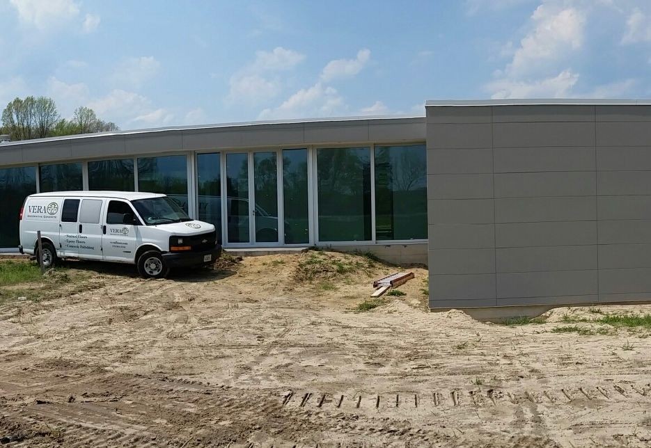 White van parked in front of a modern building under construction, surrounded by dirt and construction materials.