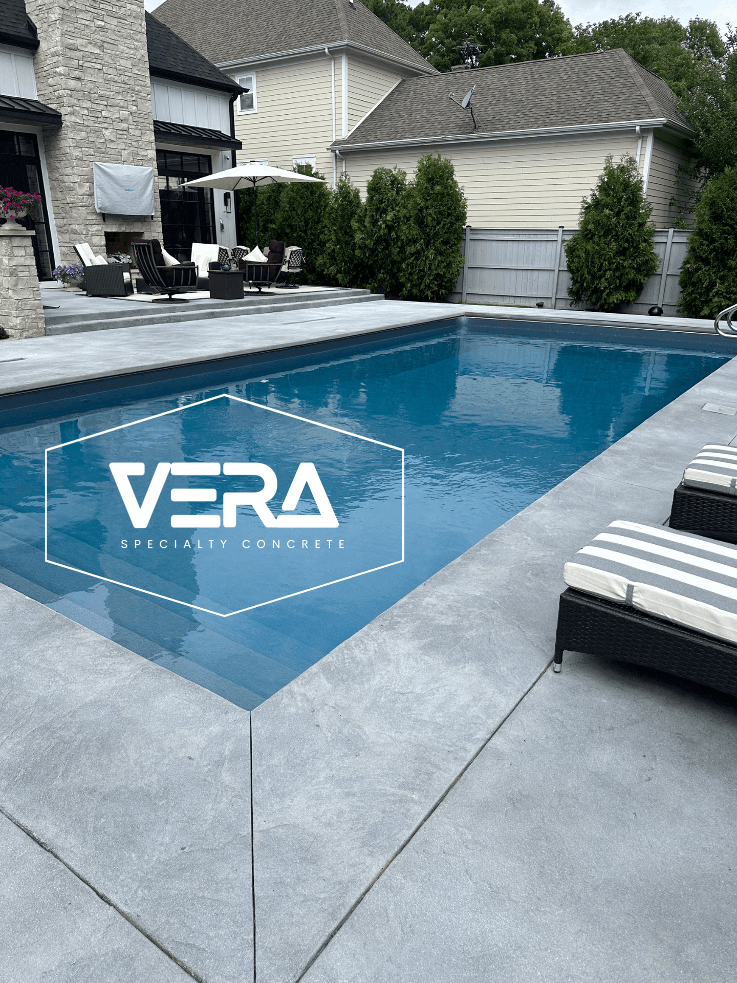 Elegant backyard pool area with lounge chairs and a modern concrete patio.